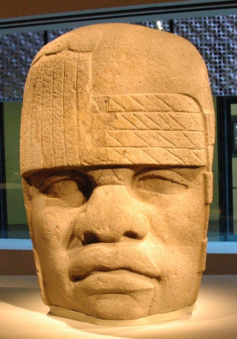 A colossal basalt Olmec head with its distinctive helmet resting on the ground