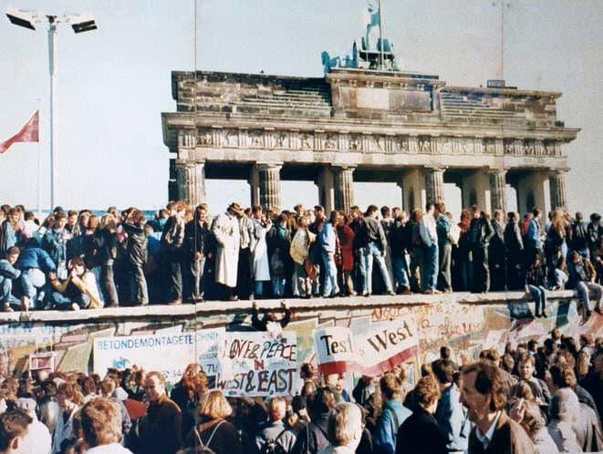 Crowds from East and West standing together on top of the Berlin Wall at the Brandenburg Gate