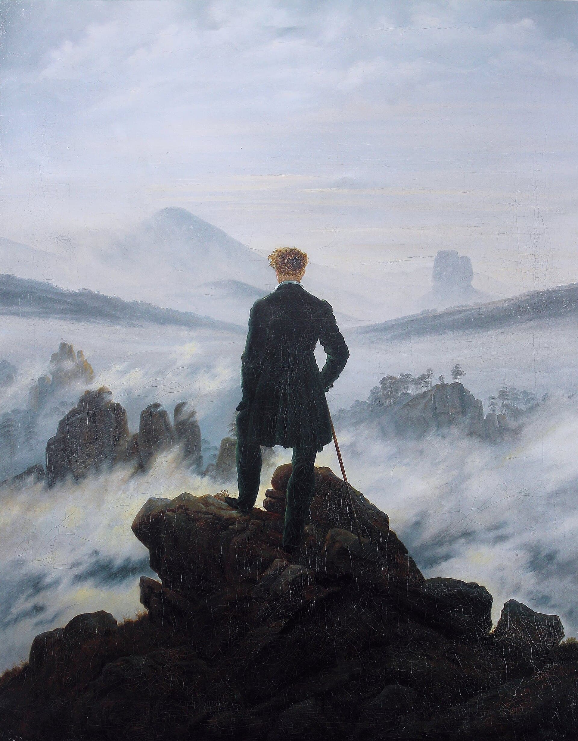A lone man in a dark green coat stands on rocks above a sea of fog